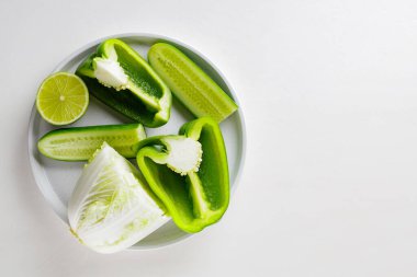 Beyaz arka planda doğranmış yeşil sebzeler ve meyveler. Beyaz tabakta yeşil diyet yemeği. Sağlıklı ve vejetaryen yemekleri. Üst Manzara. Boşluğu kopyala