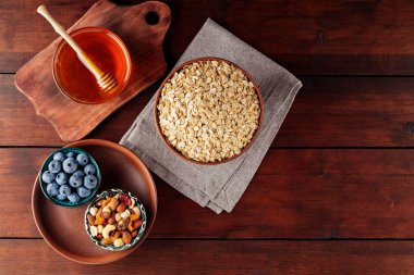 Kuru yulaf ezmesi, yabanmersini, bal ve ahşap arka planda çeşitli fındıklar. Mısır gevreği ve tahtalardaki kahvaltı için çeşitli lezzetli malzemeler. Uzayı kopyala Üst görünüm