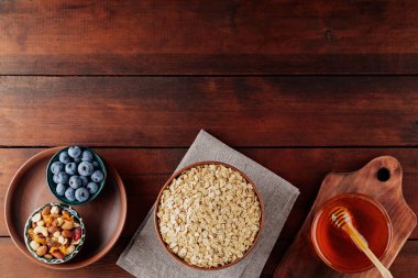 Kuru yulaf ezmesi, yabanmersini, bal ve ahşap arka planda çeşitli fındıklar. Mısır gevreği ve tahtalardaki kahvaltı için çeşitli lezzetli malzemeler. Uzayı kopyala Üst görünüm