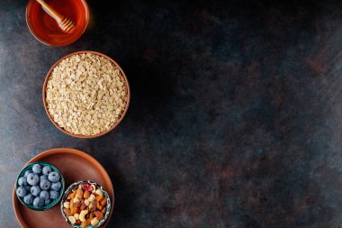 Koyu arkaplanda yulaf ezmesi, fındık, böğürtlen ve bal var. Yulaf ezmesi ve yaban mersinli sağlıklı kahvaltı için gerekli malzemeler. Uzayı kopyala Üst görünüm