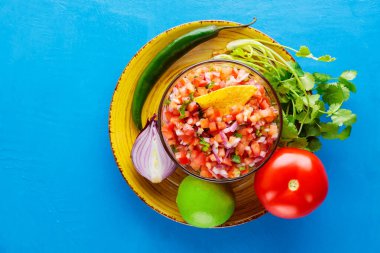 Pico de Gallo ve mavi arka plandaki malzemeler. Bir kase Meksika Pico de Gallo 'su masada. Meksika mutfağı. Üst Manzara. Boşluğu kopyala