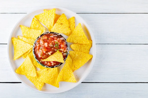 Mexican salsa sauce and nacho chips on a white plate. Tortilla chips and salsa dip in bowl on white boards. Mexican food concept. Top view. Copy space