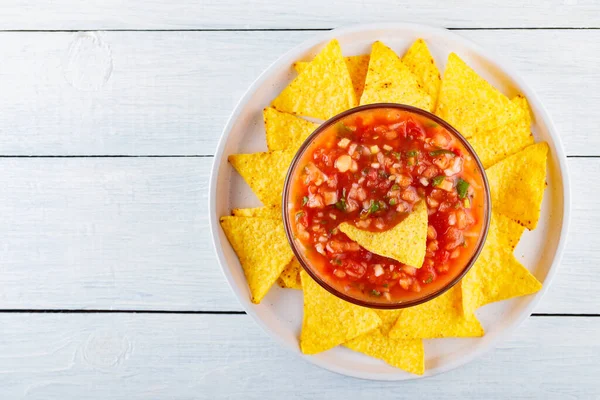 Mexican salsa sauce and nacho chips on a white plate. Tortilla chips and salsa dip in bowl on white boards. Mexican food concept. Top view. Copy space