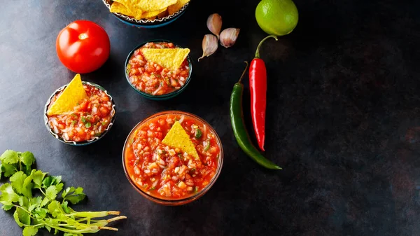 Traditional Latin American mexican salsa sauce and ingredients. Salsa sauce and nacho chips on a dark background. Mexican cuisine. Top view. Copy space