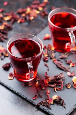 Hibiscus çayı koyu arkaplanda cam bardakta. Bir bardak kırmızı amber çayı ve tahta üzerinde kuru amber yaprağı.