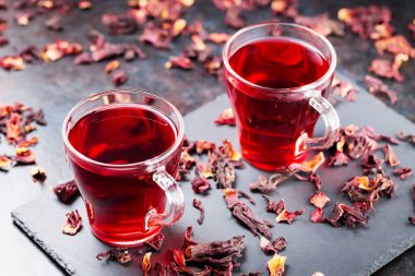Hibiscus çayı koyu arkaplanda cam bardakta. Bir bardak kırmızı amber çayı ve tahta üzerinde kuru amber yaprağı.