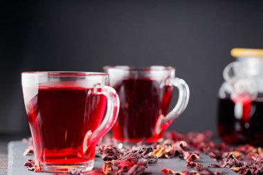 Hibiscus çayı koyu arkaplanda cam bardakta. Bir bardak kırmızı amber çayı ve tahta üzerinde kuru amber yaprağı.