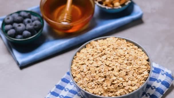 ボウルにオートミール ドライオートミール ブルーベリー ナッツと蜂蜜 灰色の背景に健康的な朝食のための成分 — ストック動画