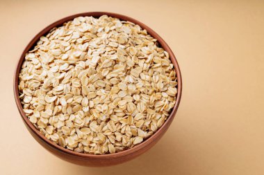 Oat flakes in a bowl. Dry rolled oatmeal on a beige background. Cooking oats porridge concept. Copy space. Top view