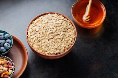 Koyu arkaplanda yulaf ezmesi, fındık, böğürtlen ve bal var. Yulaf ezmesi ve yaban mersinli sağlıklı kahvaltı için gerekli malzemeler. Üst görünüm