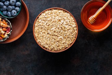 Koyu arkaplanda yulaf ezmesi, fındık, böğürtlen ve bal var. Yulaf ezmesi ve yaban mersinli sağlıklı kahvaltı için gerekli malzemeler. Üst görünüm