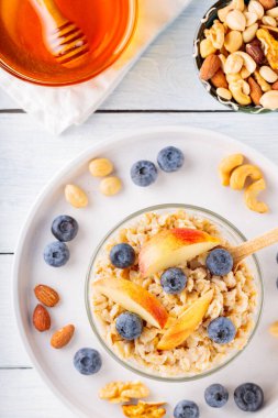 Yabanmersinli yulaf ezmesi ve kasede dilimlenmiş elma. Böğürtlenli, fındıklı ve ballı yulaf lapası. Sağlıklı kahvaltı konsepti. Üst görünüm