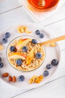 Yabanmersinli yulaf ezmesi ve kasede dilimlenmiş elma. Böğürtlenli, fındıklı ve ballı yulaf lapası. Sağlıklı kahvaltı konsepti. Üst görünüm
