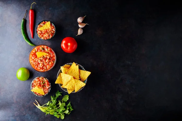 Salsa sauce and nacho chips on a dark background. Mexican salsa sauce and ingredients. Mexican food. Copy space. Top view