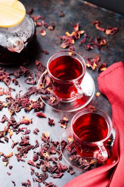 Cam bardakta Hibiscus çayı ve bordo peçete. Bir fincan amberçiçeği çayı ve koyu arkaplanda kuru amber yaprağı. Sağlıklı doğal zayıflatma içeceği.