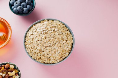 Pembe arka planda yulaf, yabanmersini, fındık ve bal. Kuru yulaf ezmesi ve diyet kahvaltı malzemeleri. Sağlıklı kahvaltı konsepti. Uzayı kopyala Üst görünüm