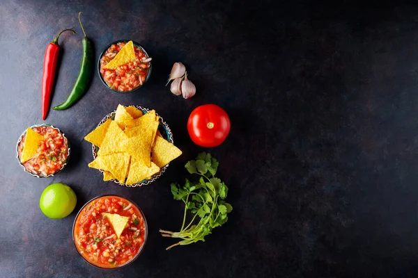Traditional Latin American mexican salsa sauce and ingredients. Salsa sauce and nacho chips on a dark background. Mexican cuisine. Top view. Copy space