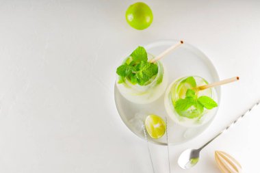 Beyaz arka planda naneli limonlu mojito kokteyli. Kokteyl için malzeme ve araç gereç yapmak. Beyaz bir tabakta iki bardak mojito. Üst Manzara. Boşluğu kopyala