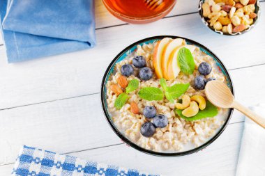 Beyaz tahtada yulaf ezmesi kasesi ve bal. Yabanmersinli yulaf ezmesi, elma dilimleri ve taze nane. Sağlıklı kahvaltı. Üst Manzara. Boşluğu kopyala