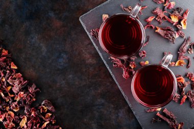 Koyu arkaplanda cam bardakta kırmızı amber çayı. Bir bardak amber çayı ve tahta üzerinde kuru amber yaprağı. Boşluğu kopyala