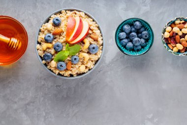 Gri arka planda sağlıklı kahvaltı malzemeleri. Yulaf ezmesi, yaban mersini, fındık, elma dilimi ve bal. Sağlıklı kahvaltı konsepti. Üst Manzara. Boşluğu kopyala