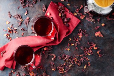 Cam bardakta Hibiscus çayı ve bordo peçete. Bir fincan kırmızı amber çayı ve koyu arkaplanda kuru amber yaprağı. Sağlıklı zayıflama içeceği. Boşluğu kopyala