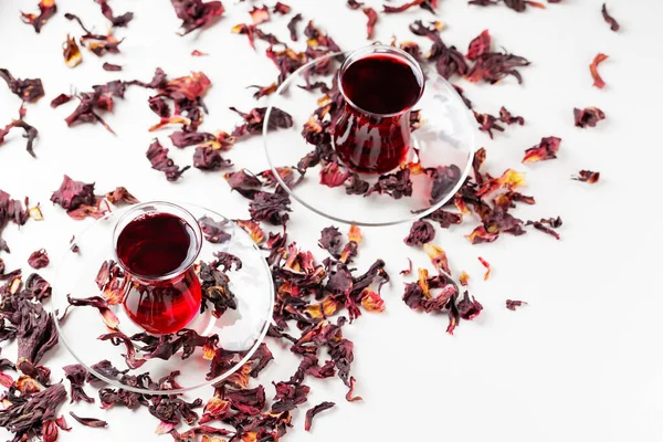 Hibiscus tea in traditional Turkish glasses on a white background. Hibiscus tea and dry hibiscus petals. Top view. Copy space