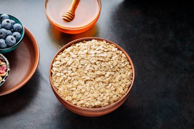 Koyu arkaplanda yulaf ezmesi, fındık, böğürtlen ve bal var. Yulaf ezmesi ve yaban mersinli sağlıklı kahvaltı için gerekli malzemeler. Üst görünüm
