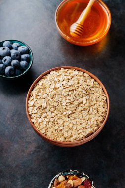 Koyu arkaplanda yulaf ezmesi, fındık, böğürtlen ve bal var. Yulaf ezmesi ve yaban mersinli sağlıklı kahvaltı için gerekli malzemeler. Üst görünüm
