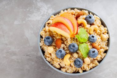 Yabanmersinli yulaf ezmesi, elma dilimleri ve fındıklı. Gri arka planda bir kase yulaf lapası. Sağlıklı beslenme, diyet, vejetaryen gıda konsepti. Uzayı kopyala Üst görünüm