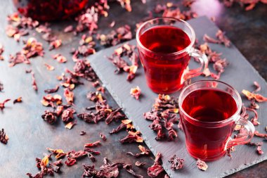 Koyu arkaplanda cam bardakta kırmızı amber çayı. Bir bardak amber çayı ve tahta üzerinde kuru amber yaprağı. Boşluğu kopyala