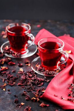 Cam bardakta Hibiscus çayı ve bordo peçete. Bir fincan amberçiçeği çayı ve koyu arkaplanda kuru amber yaprağı. Sağlıklı doğal zayıflatma içeceği.