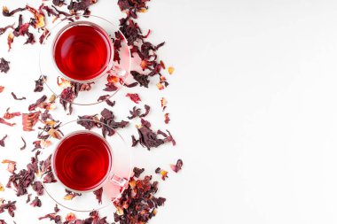 Beyaz arka planda bir fincan amberçiçeği çayı (rosella, karkade, kırmızı kuş). Hibiscus çayı ve kuru amber yaprağı. Bitkilerle birlikte idrar söktürücü içecek. Üst Manzara. Boşluğu kopyala