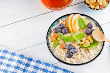 Beyaz tahtada yulaf ezmesi kasesi ve bal. Yabanmersinli yulaf ezmesi, elma dilimleri ve taze nane. Sağlıklı kahvaltı. Üst Manzara. Boşluğu kopyala