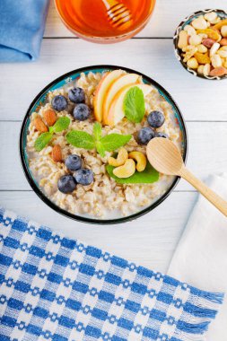 Beyaz tahtada yulaf ezmesi kasesi ve bal. Yabanmersinli yulaf ezmesi, elma dilimleri ve taze nane. Sağlıklı kahvaltı. Üst Manzara. Boşluğu kopyala