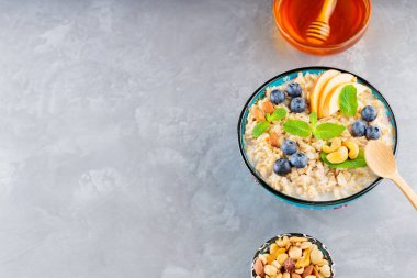 Yabanmersinli yulaf ezmesi kasesi, fındık ve ballı gri arka plan. Elmalı yulaf lapası ve taze nane. Sağlıklı kahvaltı. Üst Manzara. Boşluğu kopyala