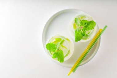Mojito kokteyli ve beyaz arka planda cam pipetler. Beyaz tepside iki bardak mojito. Yaz tatili kavramı. Boşluğu kopyala