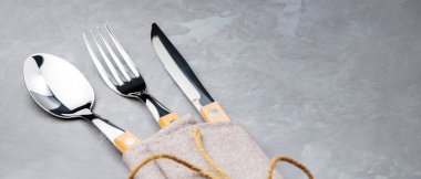 Gri arka planda çatal bıçak takımı. İplikle bağlanmış keten peçeteye kaşık, çatal ve bıçak. Masa ayarı. Boşluğu kopyala