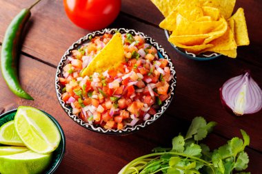 Meksika usulü Pico de Gallo salsası ve malzemeleri. Ahşap arka planda bir kase lezzetli Pico de Gallo salsası. İspanyol yemeği konsepti. Üst görünüm