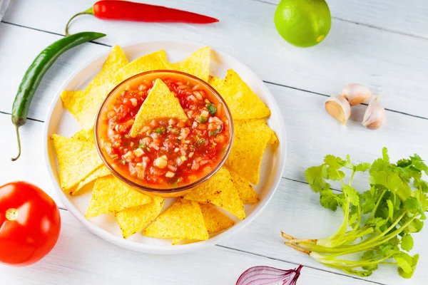 Mexican salsa sauce and nacho chips on white plate. Homemade salsa dip and ingredients on a white boards. Mexican cuisine. Top view