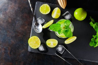 Mojito kokteyli ve koyu bir arka planda malzemeler. Kaykay tahtasında kokteyl mojito tazeliyorum. Limon ve naneli yaz kokteyli konsepti. Üst görünüm