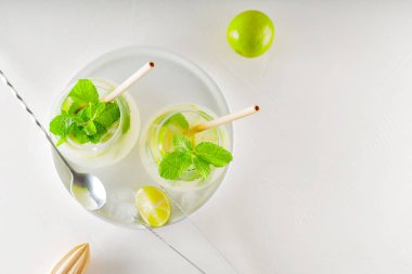 Beyaz arka planda naneli limonlu mojito kokteyli. Kokteyl için malzeme ve araç gereç yapmak. Beyaz bir tabakta iki bardak mojito. Üst Manzara. Boşluğu kopyala