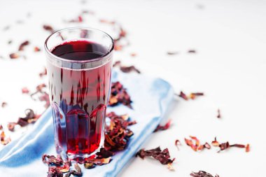 Mavi peçetede uzun bir bardakta Hibiscus çayı. Beyaz arka planda sağlıklı amberçiçeği çayı ve kuru amber yaprağı. Boşluğu kopyala
