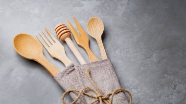 Gri arka planda ahşap çatal bıçak takımı. İplikle bağlanmış keten peçeteye bal için kaşık, çatal ve tahta sopa. Sıfır çöp masası. Boşluğu kopyala