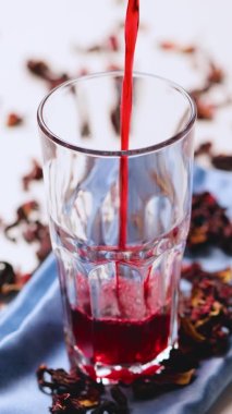 Hibiscus çayı bardağa dökülüyor. Hibiscus son moda çay yapmak için yapraklar. Mavi peçetede kırmızı amber çayı. Dikey video