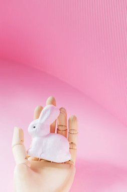 Tahta bir elde Paskalya Tavşanı. Pembe arka planda suni bir elde beyaz tavşan. Gelecekçi Paskalya konsepti. Boşluğu kopyala