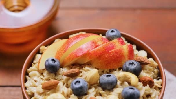 木製の背景にブルーベリー ナッツ 蜂蜜とオートミール 素朴なスタイルでリンゴ ベリー ナッツとオートミール粥 健康的な食事のコンセプト — ストック動画