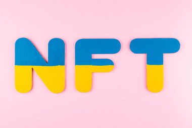 NFT (Non-Fungible Token) in Ukrainian flag colors. Blue-yellow NFT inscription on pink background. Ukraine support concept. Top view. Copy space clipart