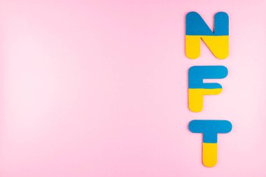 Ukrayna bayrağı renklerinde NFT (İade edilemez Token). Pembe arka planda mavi-sarı NFT yazıları var. Ukrayna destek konsepti. Üst Manzara. Boşluğu kopyala
