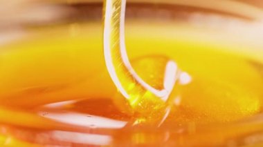 Ahşap çubuktan damlayan kalın bal, yakın plan. Bal, ahşap bir baldan cam bir kaseye dökülüyor. Sağlıklı organik bal damlıyor